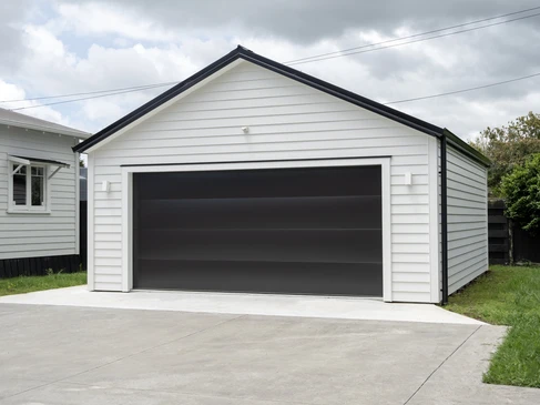 Garage résidentiel moderne avec porte sectionnelle automatique anthracite ouverte, façade en bardage composite blanc, toiture à deux pans avec bordures noires