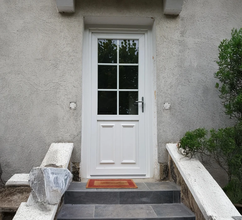 Entrée extérieure d'une habitation avec porte blanche vitrée à six carreaux dans la partie haute et deux panneaux pleins en partie basse