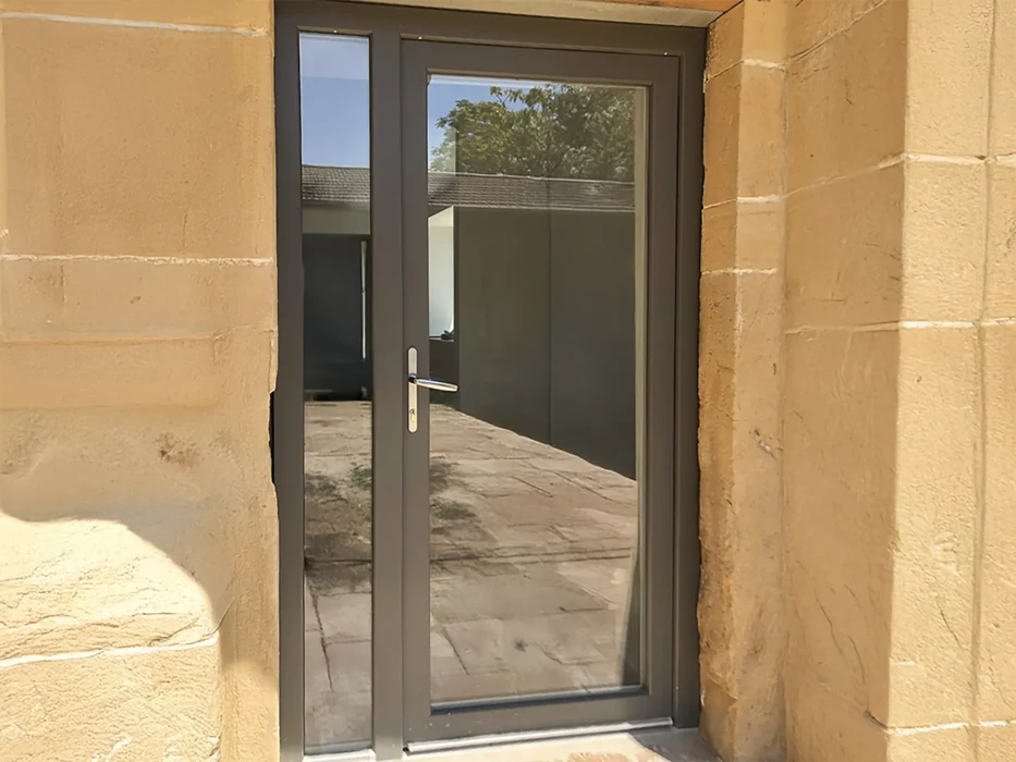 Extérieur d'une habitation avec grande baie vitrée coulissante à cadre blanc PVC installée dans mur crépi beige