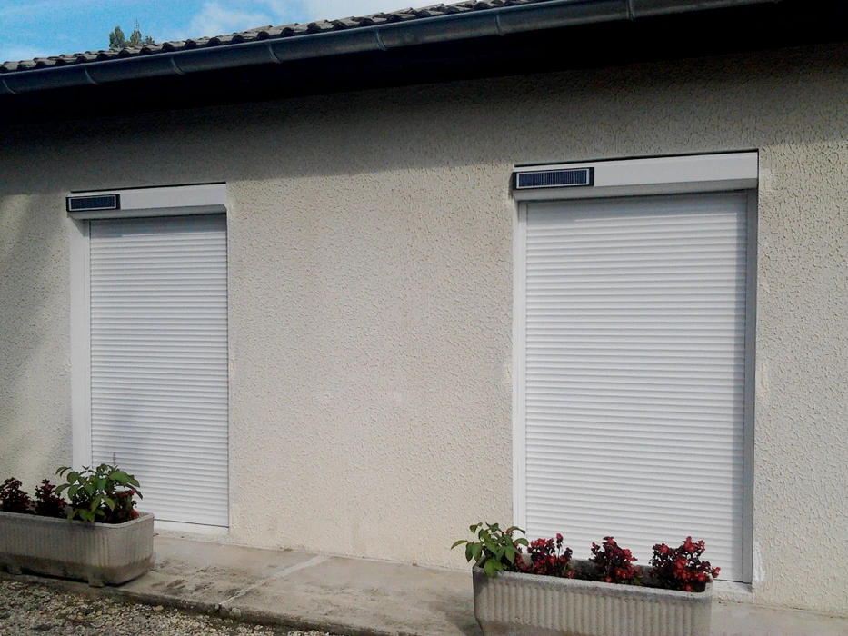 Extérieur d'une habitation avec grande baie vitrée coulissante à cadre blanc PVC installée dans mur crépi beige