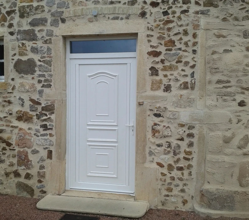 Extérieur d'une habitation avec grande baie vitrée coulissante à cadre blanc PVC installée dans mur crépi beige