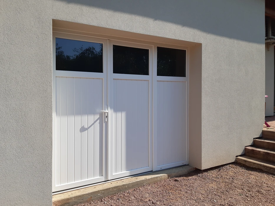 Extérieur d'une habitation avec grande baie vitrée coulissante à cadre blanc PVC installée dans mur crépi beige