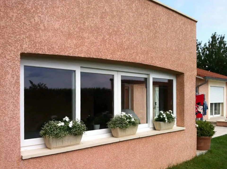 Extérieur d'une habitation avec fenêtre moderne à cadre anthracite installée dans mur crépi beige