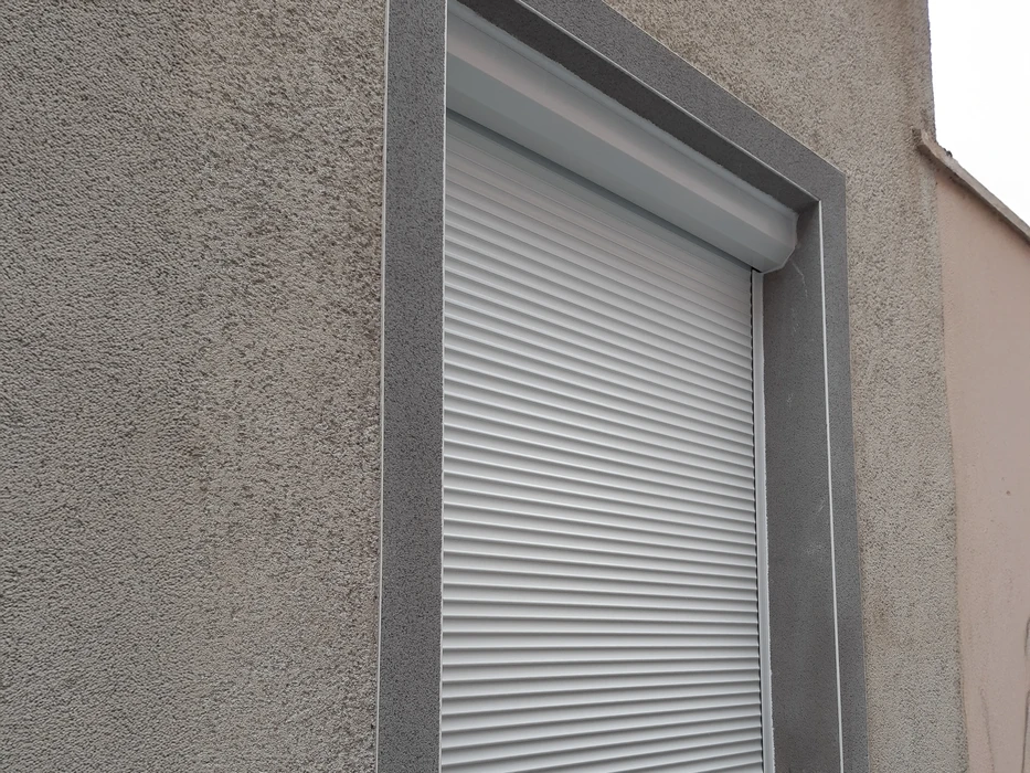 Façade extérieure d'une construction en bois avec volet roulant électrique partiellement fermé sur une fenêtre