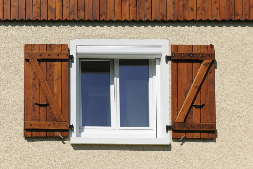 Façade extérieure d'un bâtiment avec volet roulant gris fermé, encadrement en aluminium anthracite sur mur crépi beige